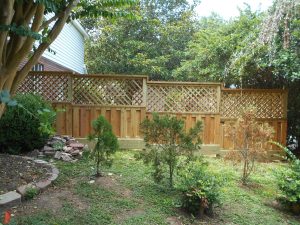 A yard with shrubs and a decorative wood fence.